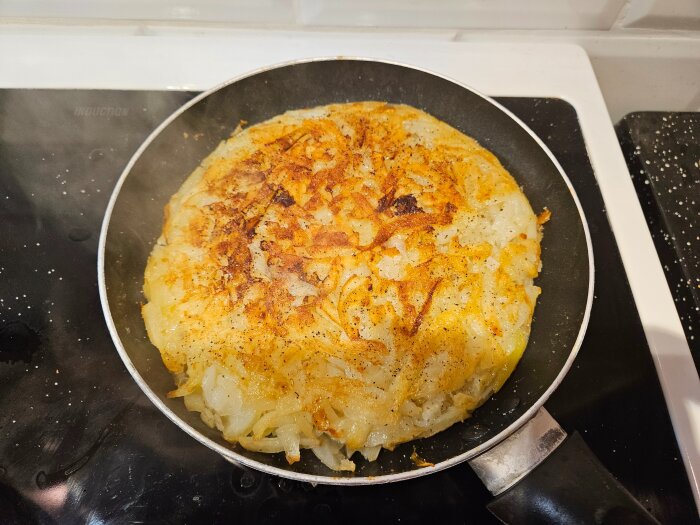 Potatis och lök som steks till en gyllene kaka i en stekpanna på spisen.