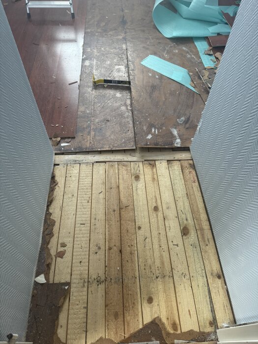 Renoveringsprojekt på övervåning med nakna träplankor, riven laminat och undergolvsmaterial, samt verktyg och byggmaterial runtomkring.