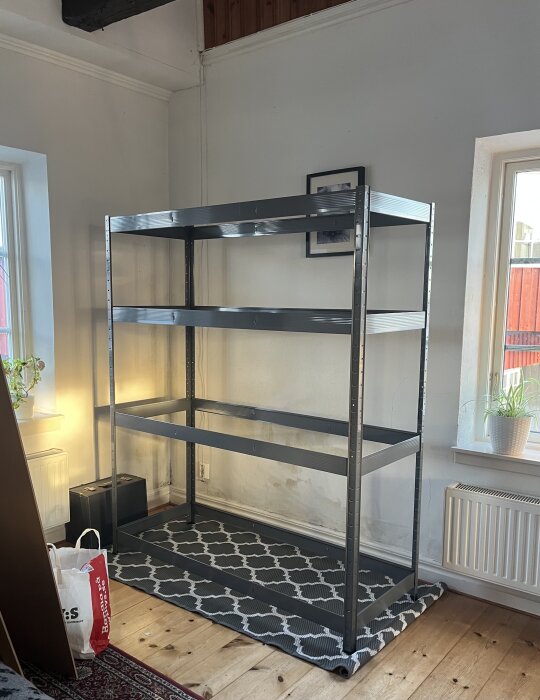 Lagerhylla utan hyllplan, med metallram, placerad mot en vägg inomhus. Golvet har en mönstrad matta under hyllan.