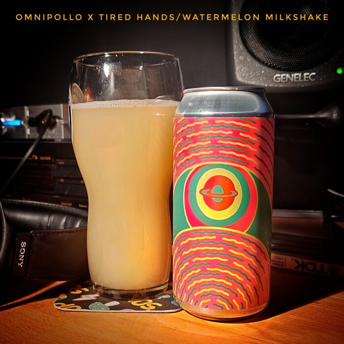 Burk och glas med Omnipollo x Tired Hands Watermelon Milkshake öl på ett bord, med färgglad etikett på burken.