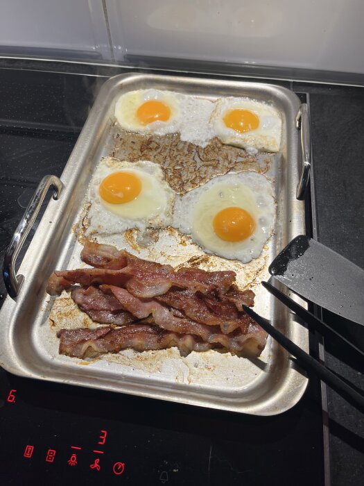 Fyra stekta ägg och bacon på en plåt på spisen, redo att serveras.