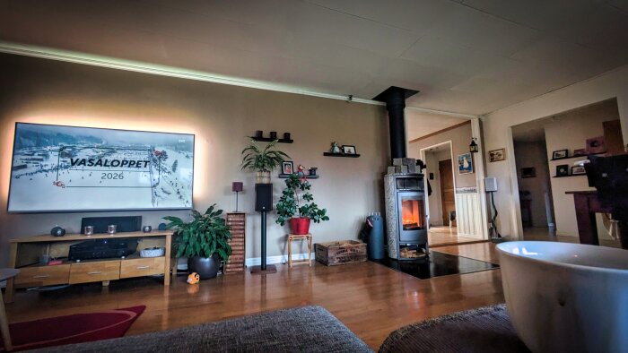 Vardagsrum med TV som visar Vasaloppet 2026, braskamin och växter. Hyllor med dekorationer och en kopp i förgrunden.