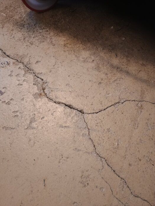 Gammalt betonggolv i lada med sprickor och slitage, del av verkstadsutrymme som planeras att slipas och målas för en fräschare yta.