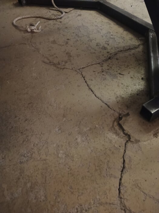 Gammalt betonggolv med sprickor i en lada, delar av golvet är slitna och skadade. Till höger syns en del av en metallkonstruktion.