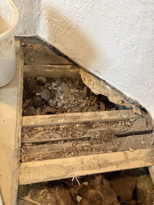 Öppet golv med synliga reglar fyllda med skräp och bråte, visar frånvarande järnvägsbalk och förstärkningar med nyare träreglar.