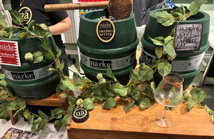 Gröna ölankare med humledekoration, tomt ölglas och etiketter från Närke Kulturbryggeri på en ölmässa.