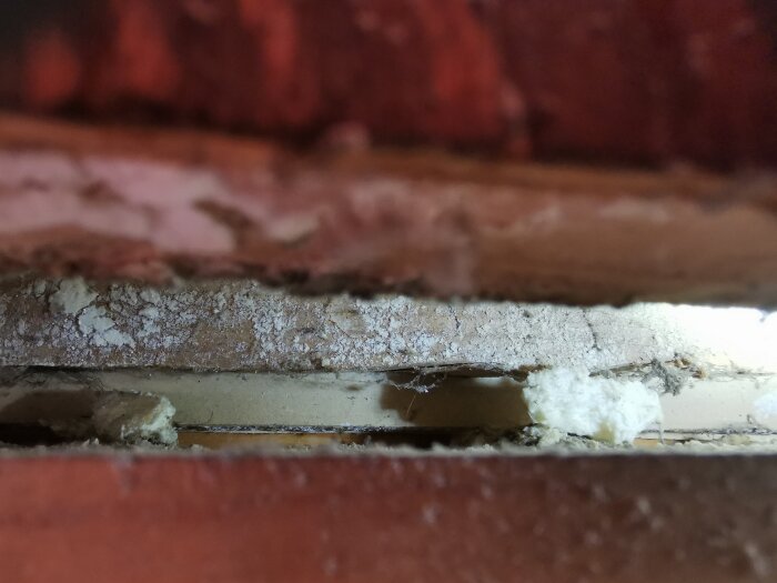 Spricka i vägg med vitt material synligt bakom borttaget dörrfoder, oklart om det är vitmögel eller mineralavlagringar.