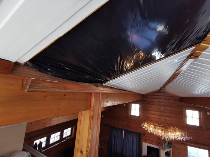 Öppnad takpanel på övervåning med exponerad limträbalk, delvis täckt av svart plastduk, vilket visar var en läcka potentiellt har uppstått.