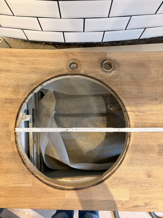 Cirkulärt hål i ekbänkskiva med mörk rand av ruttet trä synlig runt, två små runda hål ovanför. Måttband tvärs över hålet visar diameter.