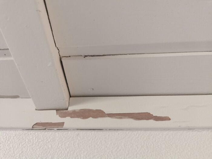 Färgflagnande i taket, synliga träytor där färg har lossnat vid skarvar på panelbrädor i ett ryggåstak.