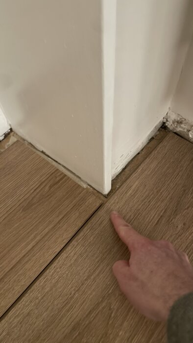 Finger pekar på glipan mellan laminatgolv och väggbräda, med tanke på hur man hanterar expansionsspalten.