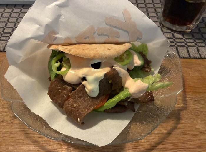 Kebab med bröd fylld med sallad, kött, sÄs och jalapeno pÄ tallrik, serverad pÄ ett dukat bord.