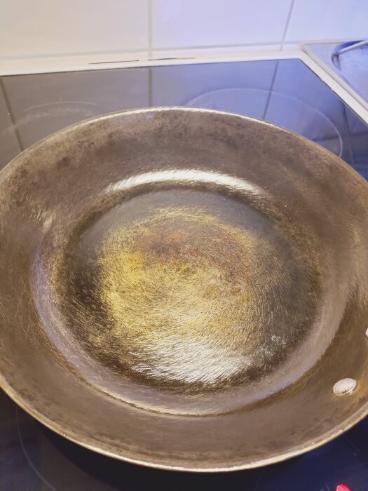 Gjutjärnspanna med gulbränd yta i mitten efter inbränning, fotograferad på en spishäll.
