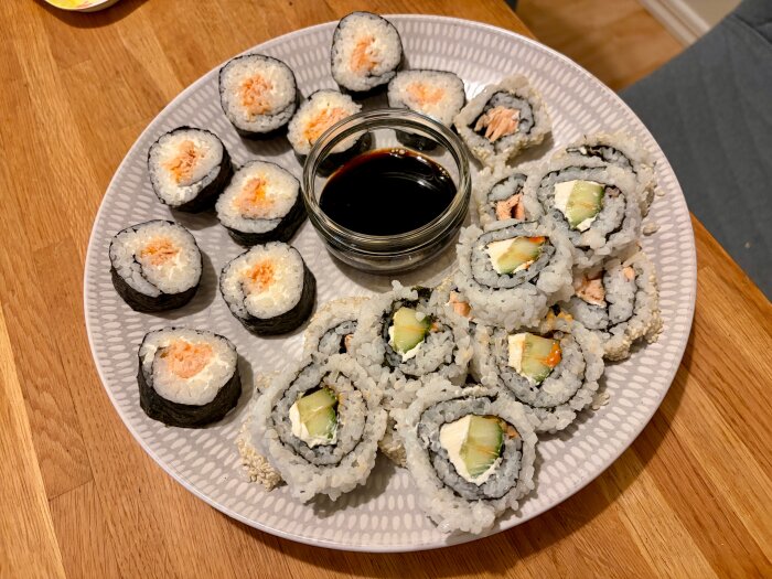 Tallrik med sushi, nÄgra med ris pÄ utsidan, serverade med sojasÄs i liten skÄl.