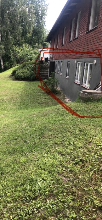 Fasadhus med murad lättbetong och puts, markerad med röd linje, omgiven av gräsmatta och buskar.