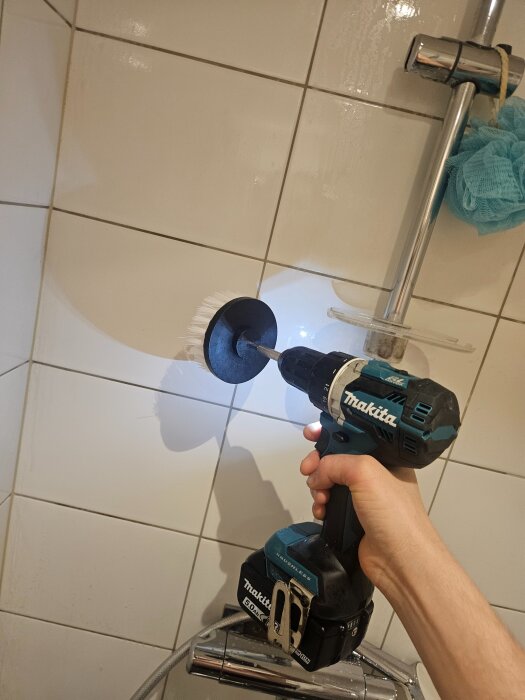 En skruvdragare med borsthuvud används för att rengöra duschens kakelvägg.