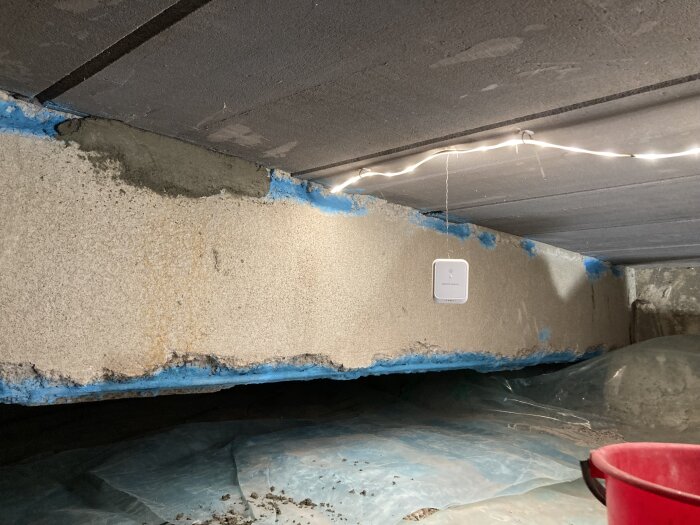 Betongbalk med blått antikorrosionsskikt i tak, omgiven av arbetsbelysning och plastskynke, före applicering av reparationsbetong.