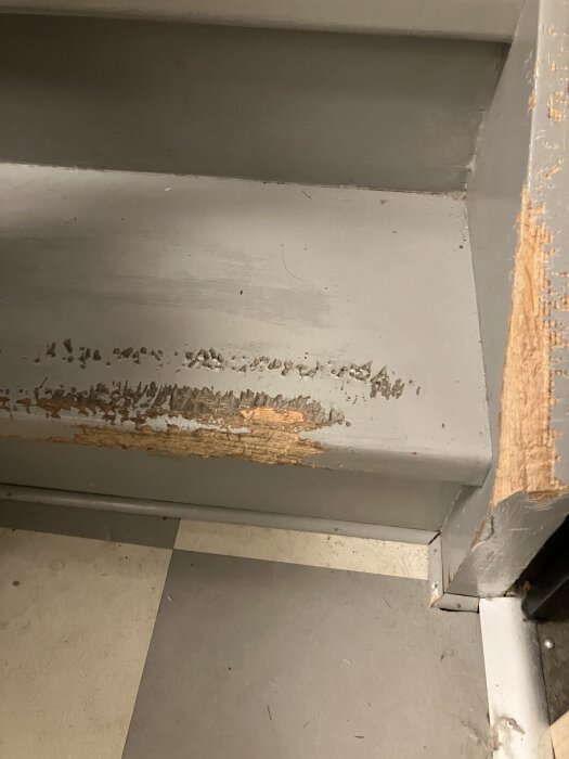 Scratched wooden stair corner with visible damage and chipped paint.