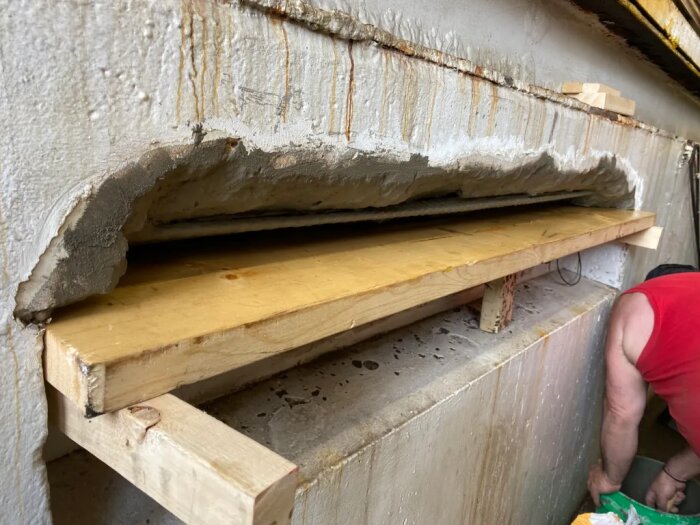 Träformstöd under ett uttag i en betongvägg, en person arbetar nedanför.