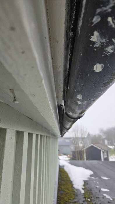 Takränna monterad på husets träfasad nära marken, med snö och gräs vid sidan av uppfarten i vintermiljö.