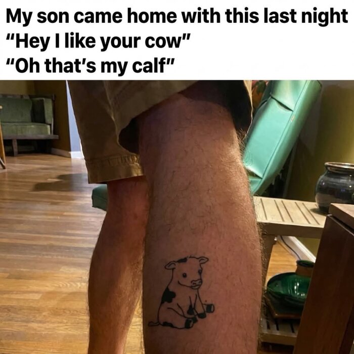 Tatuering av en tecknad kalv på en vad, inomhus med trägolv och möbler i bakgrunden.