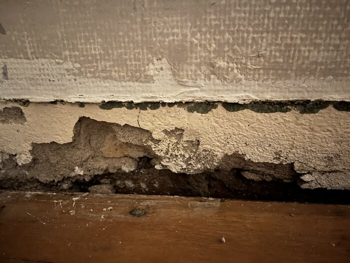 Vägg med skadat puts och fuktfläckar ovanför trälist.