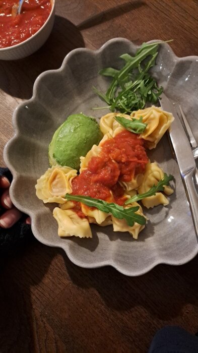 Tortellini med tomatsÄs och rucola pÄ en tallrik, serverat med grön Àrtpuré.