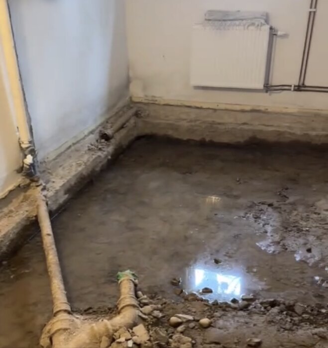 Vatten i ett öppet grundutrymme med exponerad jord och rör, där risken för sättningsskador på grund av erosion är en oro.