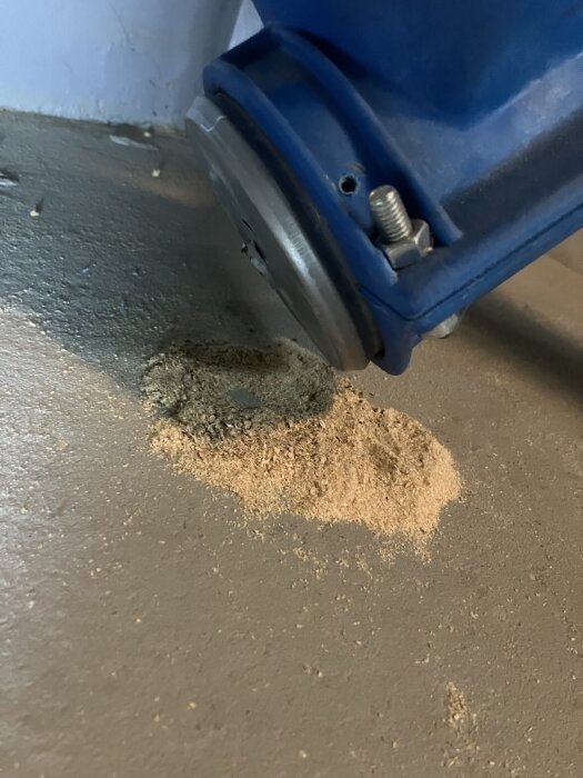 Blå pelletsmatningsdel med träpellets på golvet, möjligt läckage från CTC Ekoflex panna.