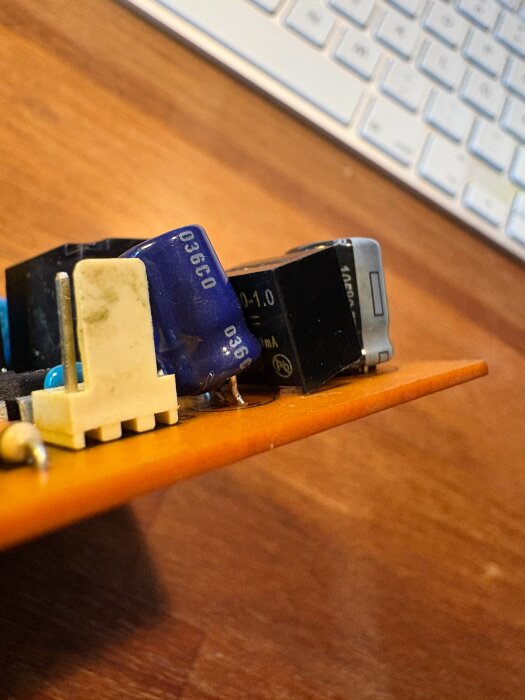 Kretskort med elektroniska komponenter, bland annat kondensatorer, liggande på ett bord med tangentbord i bakgrunden.