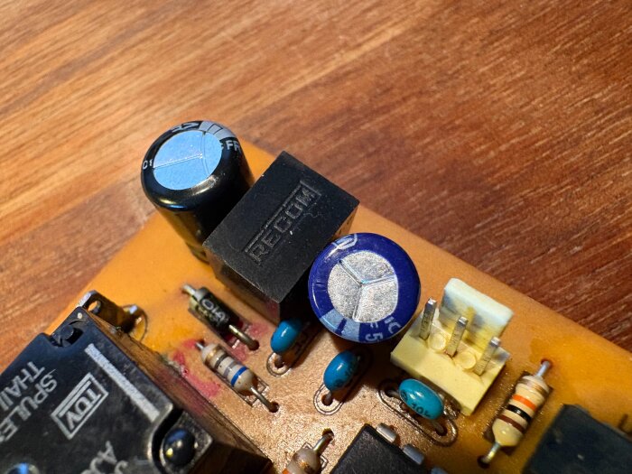 Kretskort med elektroniska komponenter som kondensatorer, motstånd och en transformator, på en träyta.