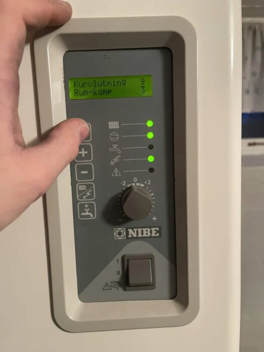 Kontrollpanel på en Nibe bergvärmepump med inställningar för kurvlutning och rumskompensering, vredinställning synlig.