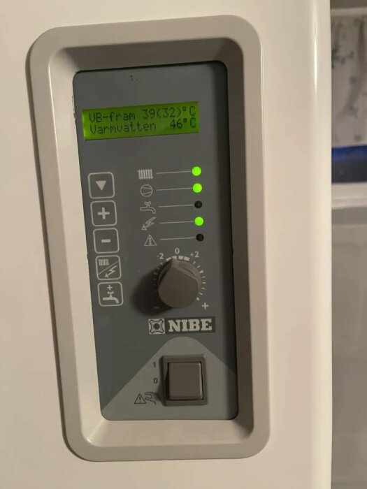 Nibe bergvärmepump kontrollpanel med temperaturreglage. Display visar UB-fram 39°C, Varmvatten 46°C och har blinkande blixtsymbol.