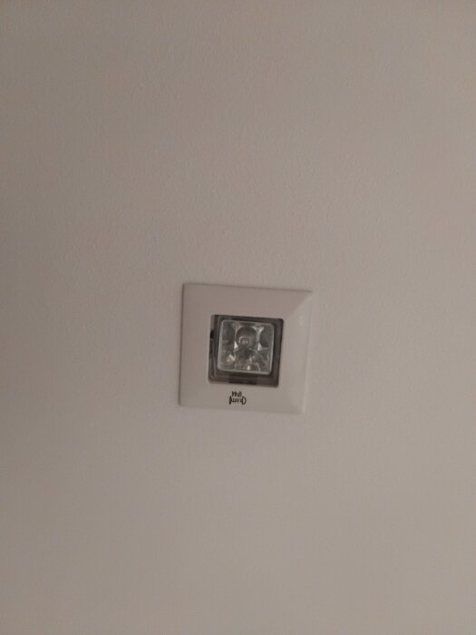 Fyrkantig spotbelysning installerad i taket, omgiven av en vit ram, i behov av ersättning.
