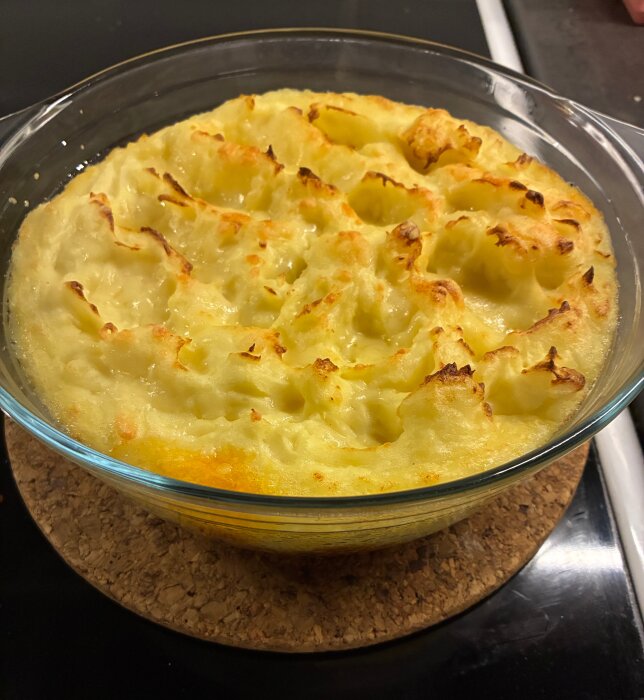 Shepherd's Pie i en glasform, täckt med gyllenbrun potatismos, på ett korkunderlägg.