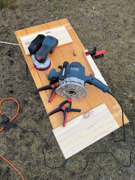 Träbord med slipmaskin, trästycken och träram på grönt gräs. Verktyg för att bygga väggmonterade sängbord.