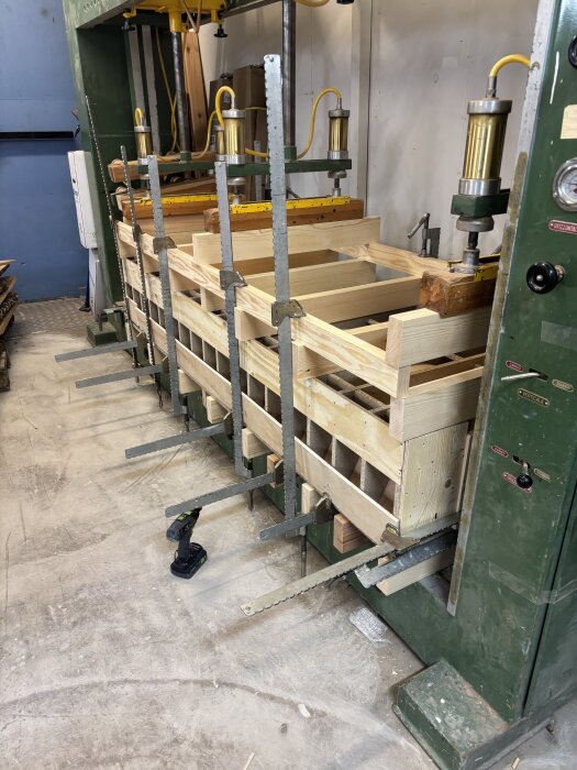 Byggpress med trästycken fastklämda, används för att limma böjd lucka i verkstadsmiljö.