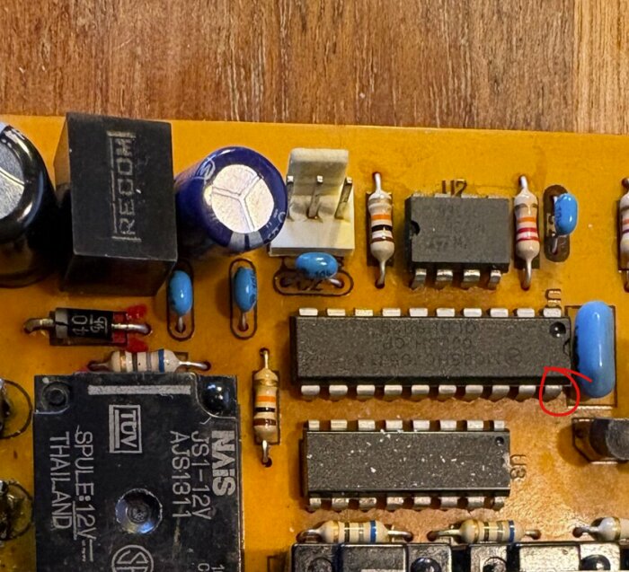 Elektroniskt kretskort med flera komponenter, inklusive motstånd och kondensatorer, på en träyta. En komponent verkar vara markerad med en röd cirkel.