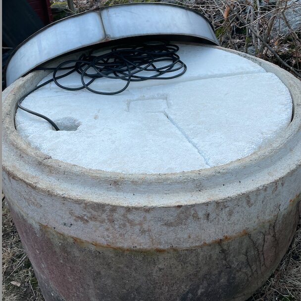 Äldre frigolitskiva på betongbrunn, delvis skadad, med en svart sladd ovanpå.