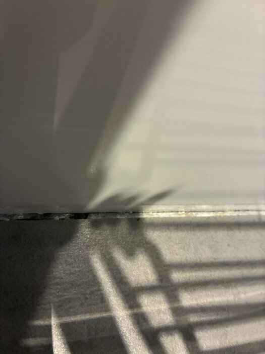 Bilden visar en närbild av fogen mellan vägg och golv i ett badrum, där fogen ser mörknad ut, kanske på grund av fukt.