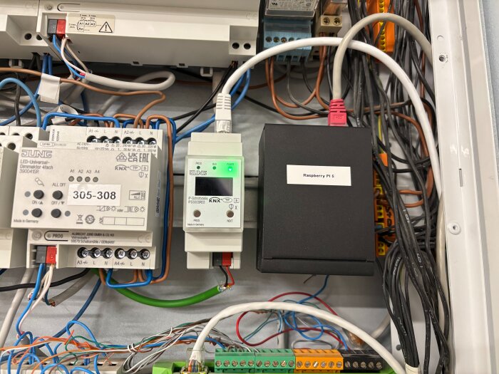Raspberry Pi 5 med Waveshare PoE Hat installerat i elskåp, omgiven av kablar och andra elektriska komponenter.