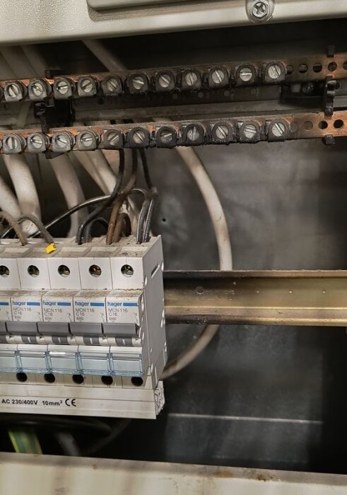 Elcentral med blandade säkringsfabrikat och kablar, något rostiga skenor.