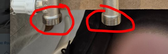 Två exponerade vattenanslutningar under ett handfat, markerade med röda cirklar.