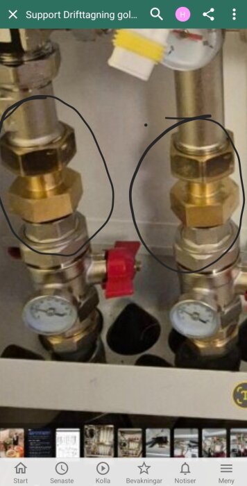 Två guldfärgade ventilkopplingar med tryckmätare och röda vred syns närbild på vad som verkar vara en del av ett rörsystem.