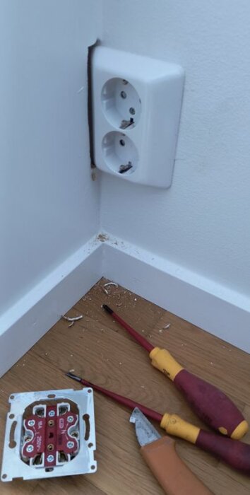 Exempel på ojordad ELKO RS-uttag monterat i vägg med verktyg och skräp på golvet, visar exakt urtagning för elektriskt arbete.