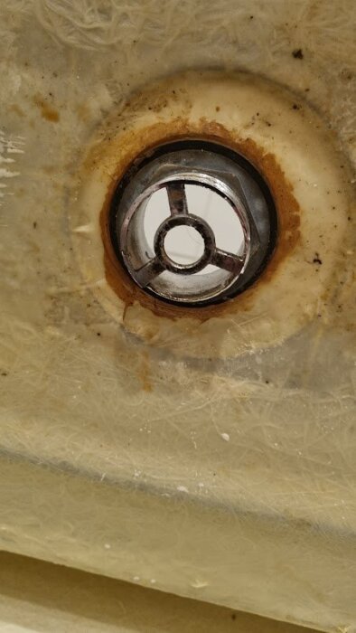 Trasig bottenventil i badkar med rostfläckar och ansamlat skräp runt kanterna, fjädern saknas vilket orsakar problem med att stänga ventilen.
