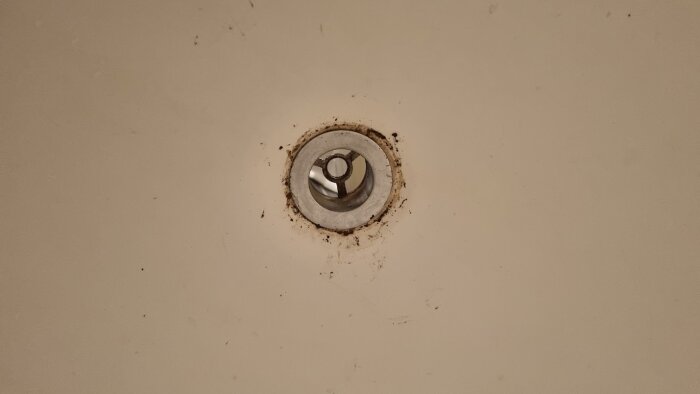 Bottenventil i ett badkar med slitage runt kanterna och smuts synligt. Ventilen verkar trasig och svår att skruva ur.
