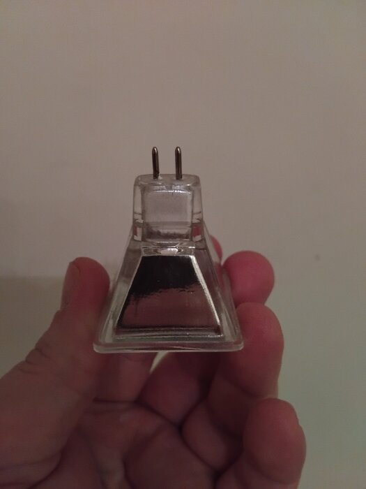 En hand håller en transparent plastkontakt med två stift mot en ljus bakgrund.