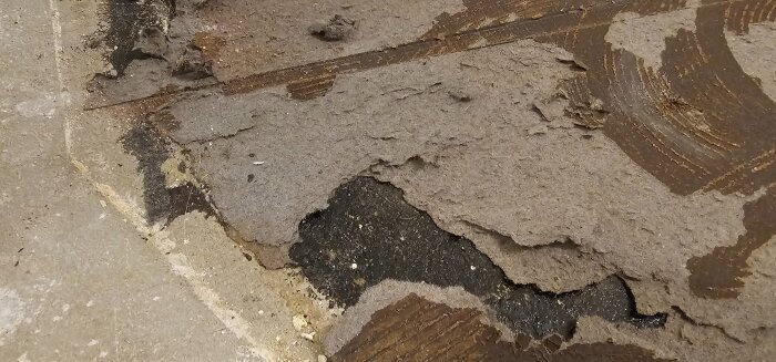Rivning av plastmatta på golv, visar lager av papp och lim på betongplatta.