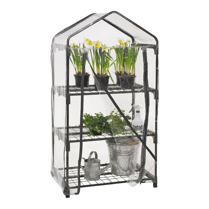 Litet växthus med genomskinligt plastskydd, tre hyllplan med blommor i krukor, grön växt i mittsektionen, och en vattenkanna på bottenplan.